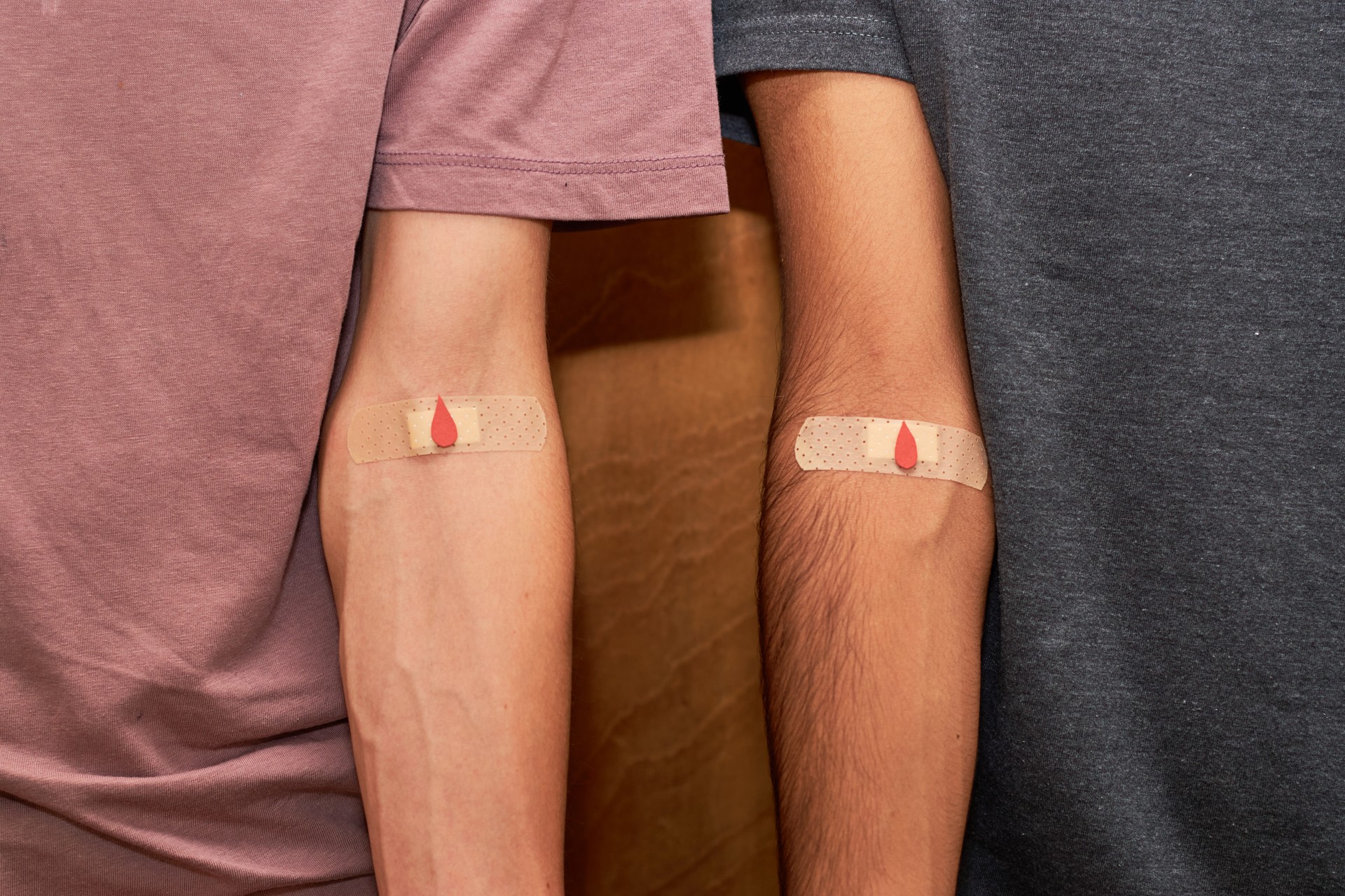 Blood donorship. Two arms with taped patch after giving blood with red drop